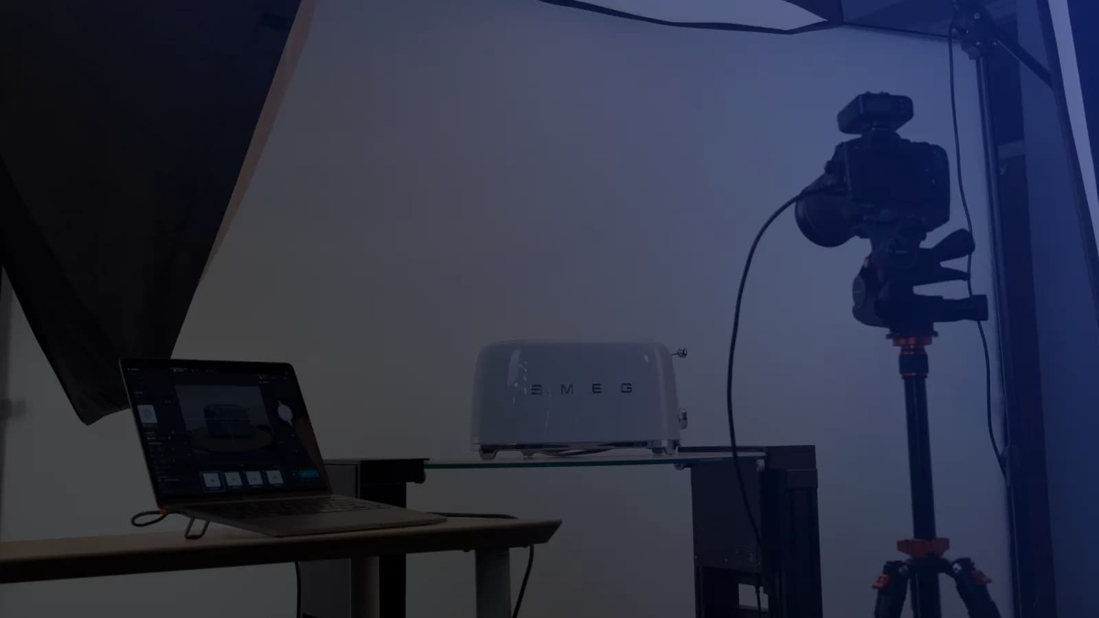 Set di fotografia di prodotto in tethering: un laptop con il software di acquisizione accanto a una fotocamera su treppiede e un prodotto su un ripiano di vetro