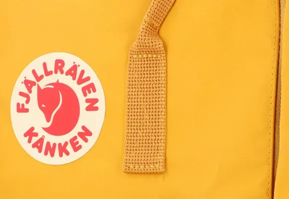 Primo piano del logo e dello spallaccio di uno zaino Kanken giallo
