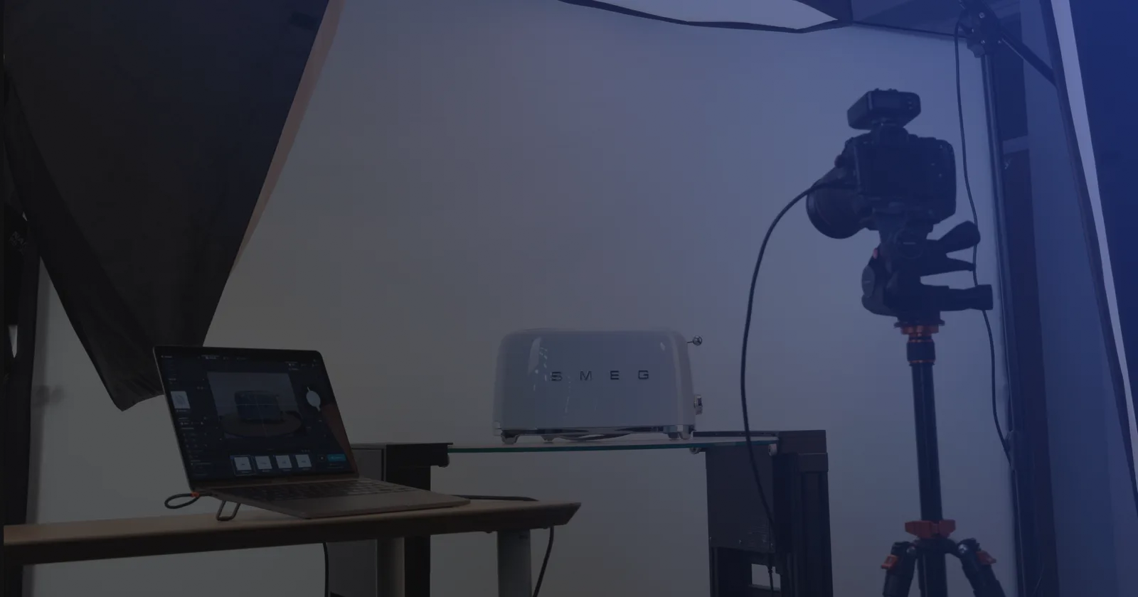 Set di fotografia di prodotto in tethering: un laptop con il software di acquisizione accanto a una fotocamera su treppiede e un prodotto su un ripiano di vetro