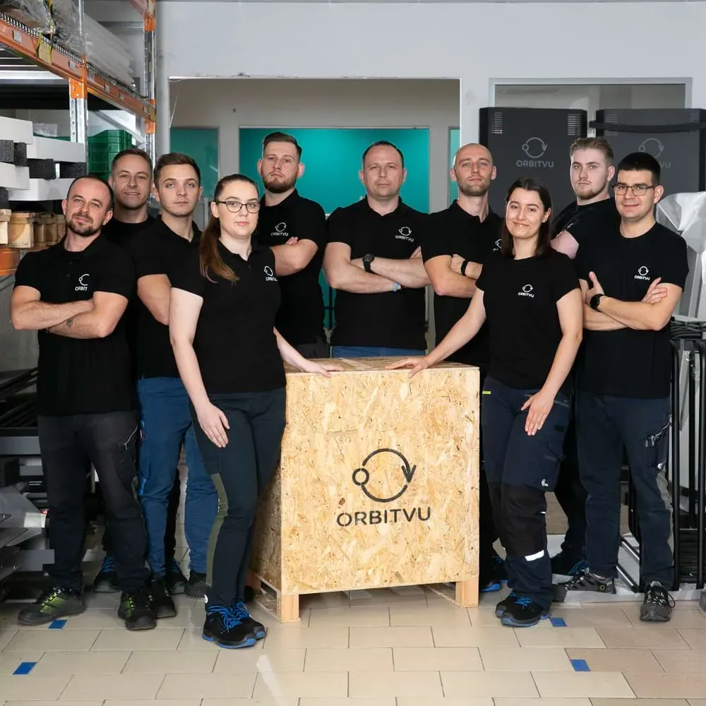 Team di produzione e logistica Orbitvu in posa con una cassa in legno marchiata